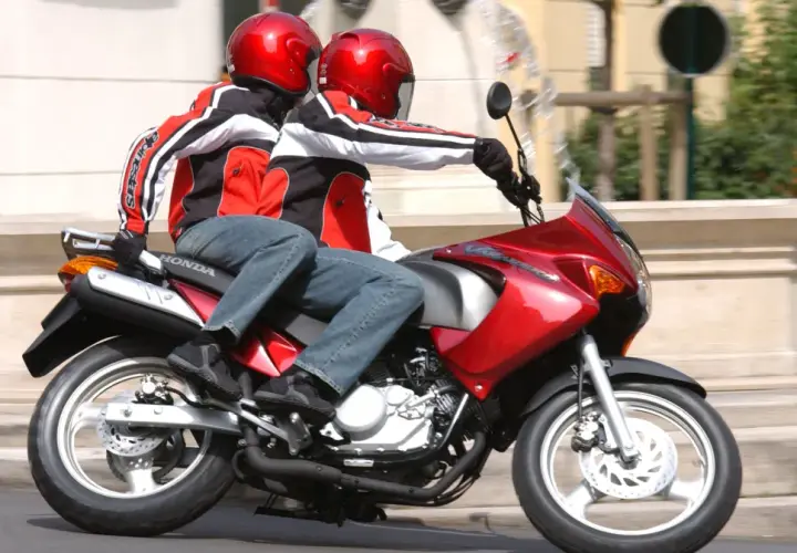 Dwie osoby w kaskach i kurtkach jadą na czerwonym motocyklu. To idealny sposób na zdobycie prawa jazdy na motor 125.