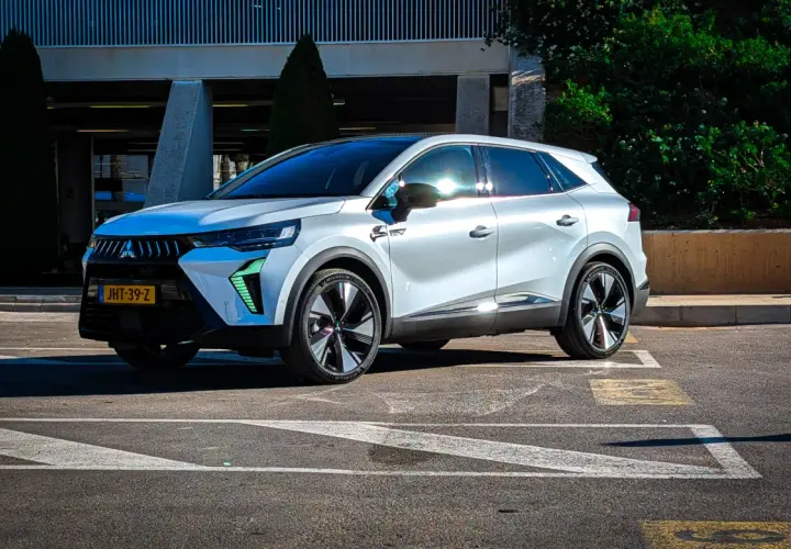 Nowy Mitsubishi Grandis w białym kolorze, zaparkowany na parkingu przed budynkiem.