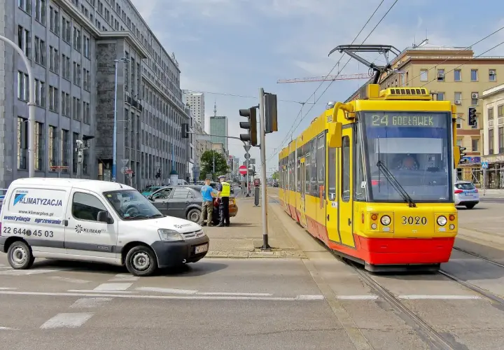 Żółty tramwaj z numerem 24 Gocławek ma pierwszeństwo na skrzyżowaniu, podczas gdy policjanci rozmawiają z kierowcą białego vana.