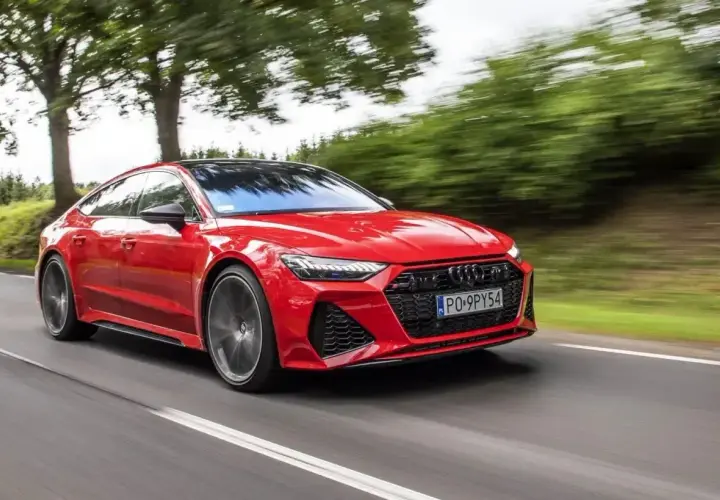 Czerwony Audi RS7 Sportback pędzi po drodze, otoczony zielenią drzew.