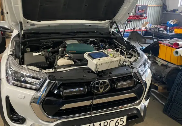 Biały Toyota Land Cruiser Prado w warsztacie, z otwartą maską i podłączonym sprzętem diagnostycznym.