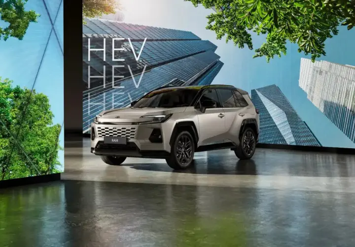 Srebrny SUV z napisem HEV na tle nowoczesnych budynków i zieleni.
