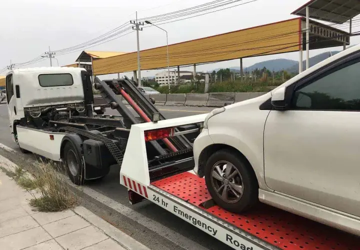 Pomoc drogowa w akcji: białe auto jest ładowane na lawetę. Widać mechanizm, jak holować auto, by bezpiecznie przetransportować pojazd.