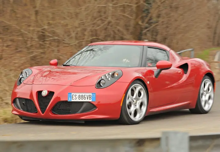 Czerwona Alfa Romeo 4C pędzi po krętej drodze, jej sportowy design przyciąga wzrok.