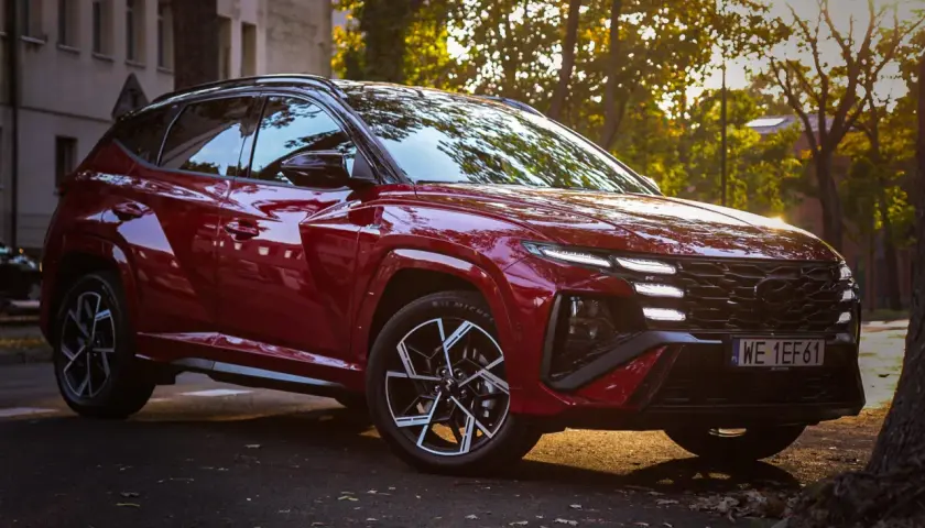 Czerwony Hyundai Tucson hybryda zaparkowany przy ulicy, oświetlony zachodzącym słońcem.