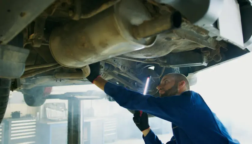 Mechanik w niebieskim kombinezonie bada podwozie auta, używając latarki. To typowa scena z warsztatu, gdzie każdy szczegół, jak ten z p0420, jest ważny.