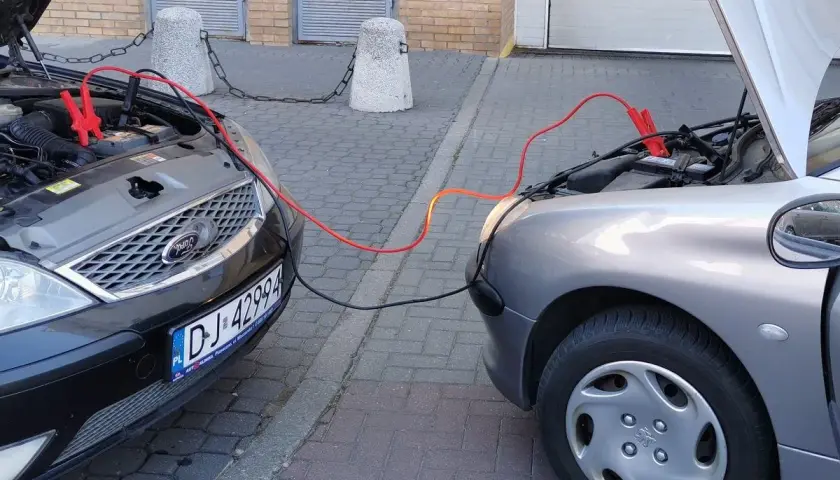Kable rozruchowe łączą dwa samochody. Czerwony to plus, czarny minus. Pomoc w awaryjnej sytuacji.