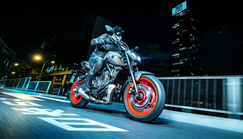 Motocyklista na szarym Yamaha MT-07 z pomarańczowymi felgami pędzi nocą przez miasto. Dane techniczne tego modelu są imponujące.