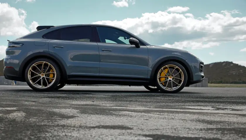 Szary Porsche Cayenne Turbo GT z żółtymi zaciskami hamulcowymi na złotych felgach, zaparkowany na pustej drodze z górzystym krajobrazem w tle.