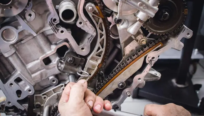 Mechanik pracuje przy rozrządzie silnika. Zbliżenie na łańcuch rozrządu i napinacz. Objawy zużytej poduszki silnika mogą być różne.