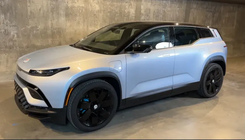 Srebrny elektryczny SUV Fisker Ocean z czarnym dachem i czarnymi felgami stoi na betonowym podłożu.