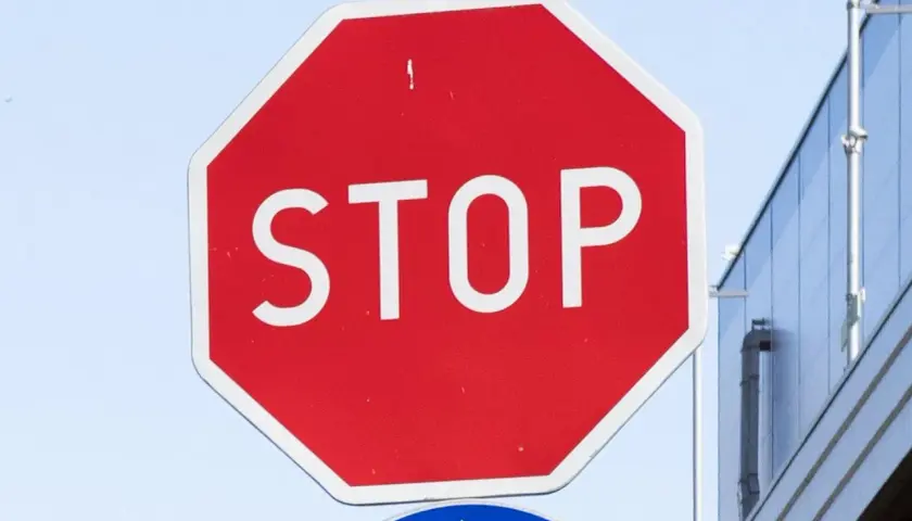 Czerwony znak stop z białym napisem "STOP" na tle nieba i budynku.