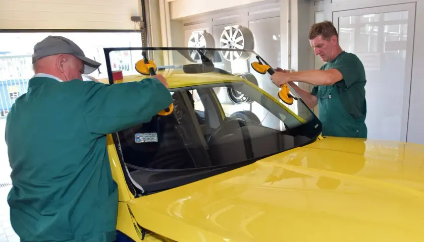 Dwóch mechaników montuje przednią szybę w żółtym samochodzie. Sprawdź autoglass cennik usług.