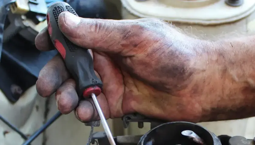 Brudna ręka mechanika przykręca śrubę, kontynuując wymianę linki hamulca ręcznego.