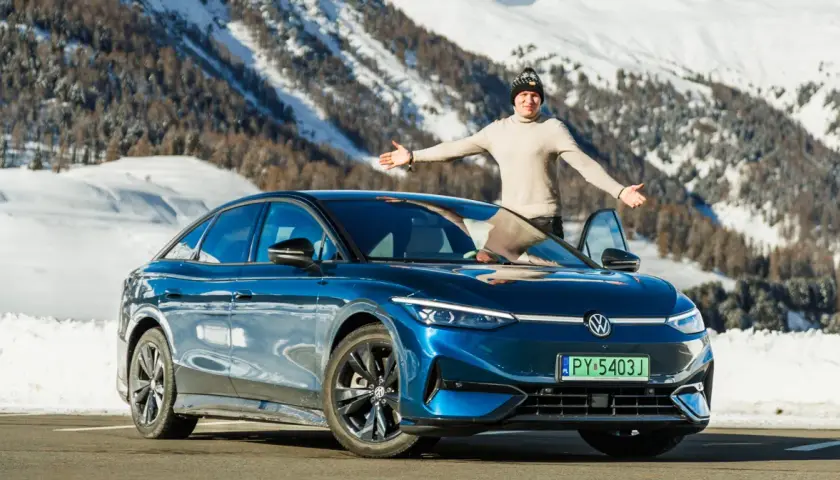 Mężczyzna z otwartymi ramionami stoi obok lśniącego, niebieskiego VW ID.7 na tle ośnieżonych gór.