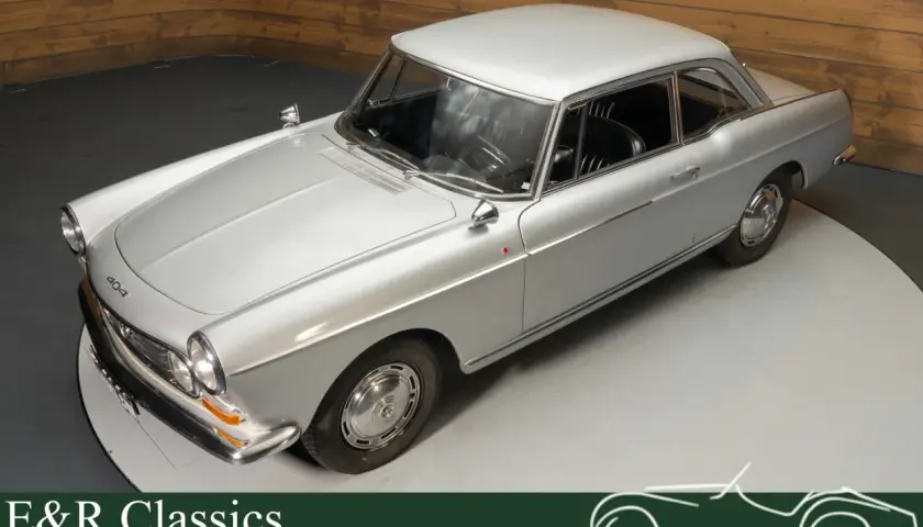 Elegancki, srebrny Peugeot 404 coupe z lat 60. na obrotowej platformie. Klasyka motoryzacji.