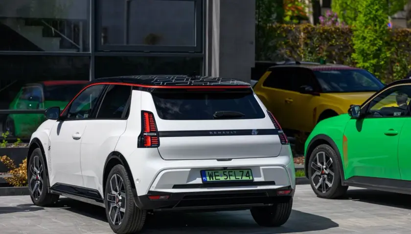 Biały Renault 5 e-tech z czarnym dachem i czerwonymi akcentami stoi obok zielonego i żółtego samochodu.