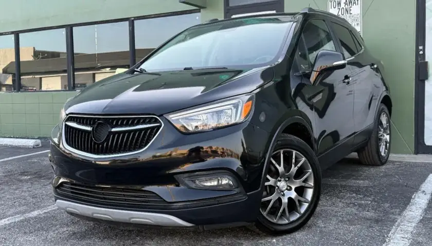 Czarny Buick Encore lśni w słońcu, zaparkowany przed zielonym budynkiem.