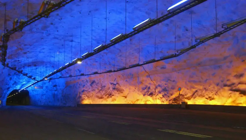 Wnętrze najdłuższego tunelu na świecie, oświetlone niebieskim i pomarańczowym światłem, z drogą prowadzącą w mrok.