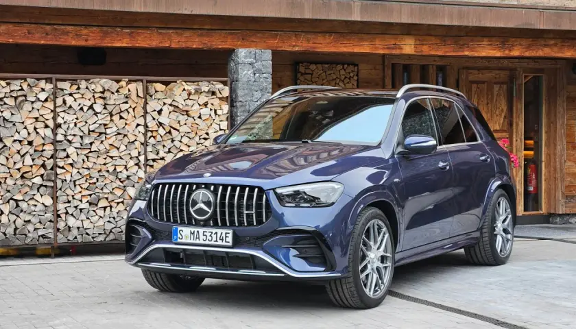 Elegancki, granatowy Mercedes GLE 53 AMG zaparkowany przed drewnianym domem z ułożonym drewnem.