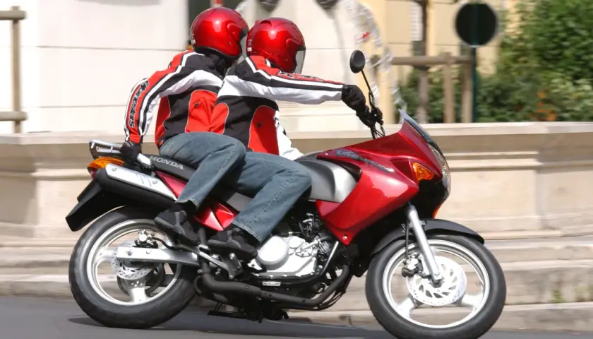 Dwie osoby w kaskach i kurtkach jadą na czerwonym motocyklu. To idealny sposób na zdobycie prawa jazdy na motor 125.
