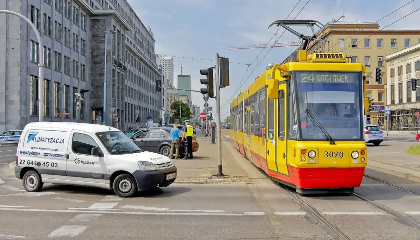 Żółty tramwaj z numerem 24 Gocławek ma pierwszeństwo na skrzyżowaniu, podczas gdy policjanci rozmawiają z kierowcą białego vana.