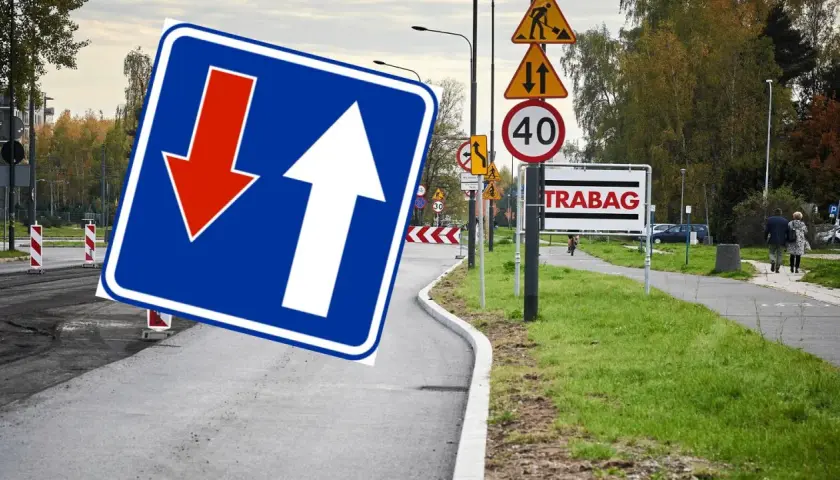 Znak D5 z białymi strzałkami, jedna w górę, druga w dół, na niebieskim tle. Obok znaki drogowe i tablica "TRABAG".