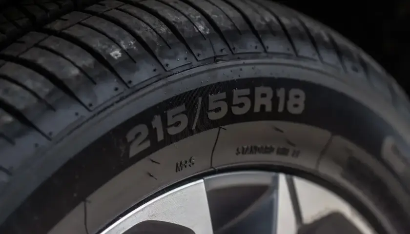 Zbliżenie na oponę z widocznym rozmiarem 215/55R18. Na boku opony można dostrzec oznaczenia dotyczące daty produkcji opony.