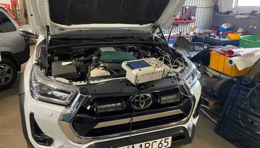 Biały Toyota Land Cruiser Prado w warsztacie, z otwartą maską i podłączonym sprzętem diagnostycznym.