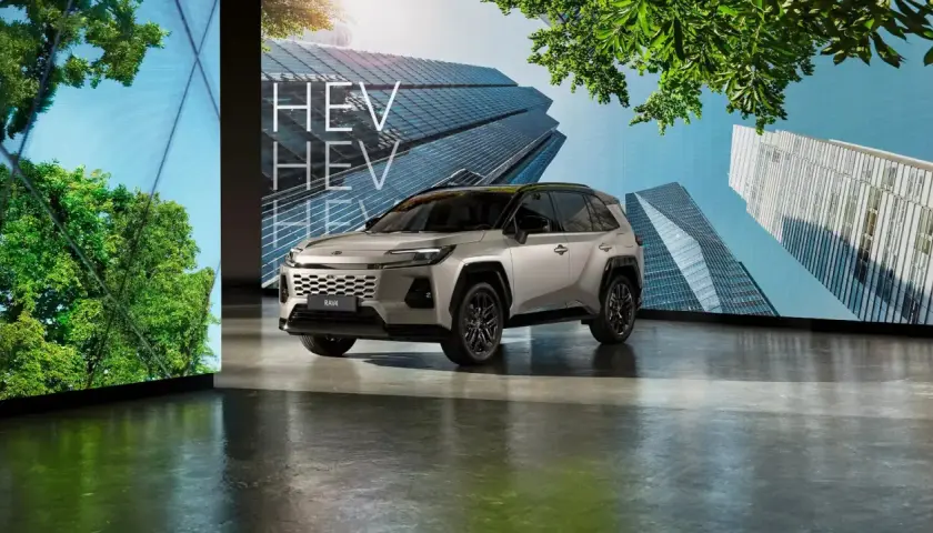 Srebrny SUV z napisem HEV na tle nowoczesnych budynków i zieleni.