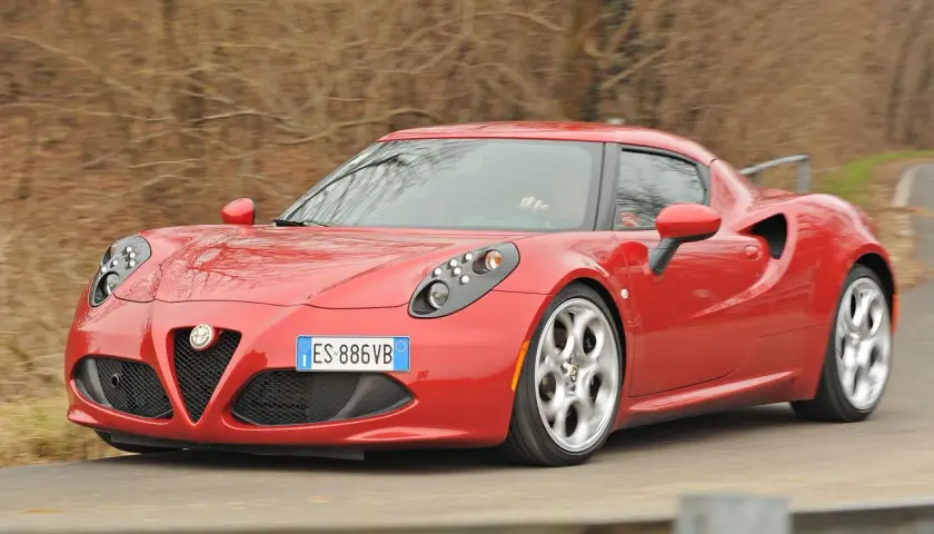 Czerwona Alfa Romeo 4C pędzi po krętej drodze, jej sportowy design przyciąga wzrok.