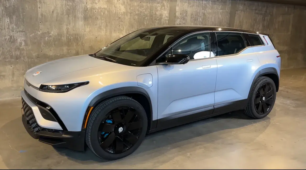 Srebrny elektryczny SUV Fisker Ocean z czarnym dachem i czarnymi felgami stoi na betonowym podłożu.