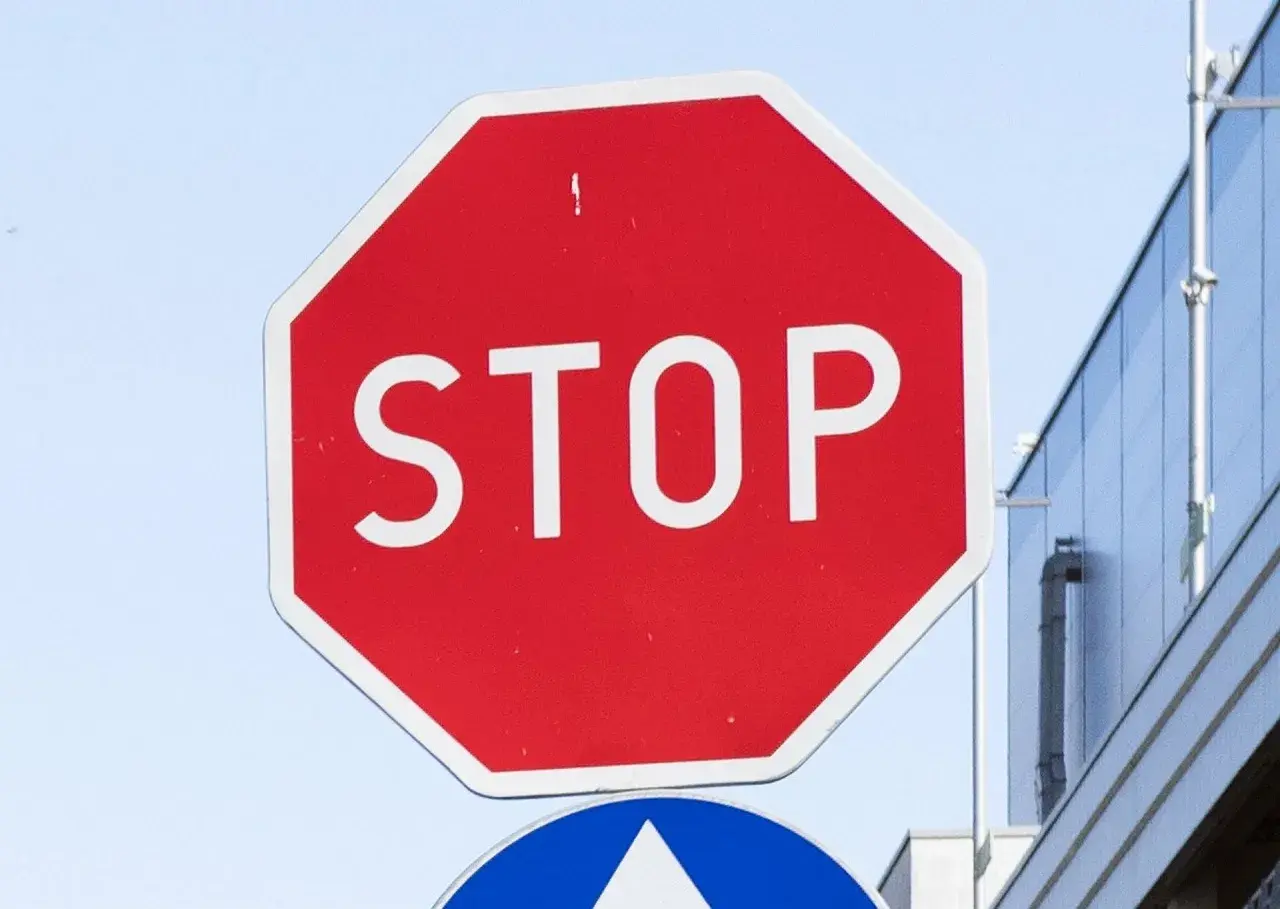 Czerwony znak stop z białym napisem "STOP" na tle nieba i budynku.