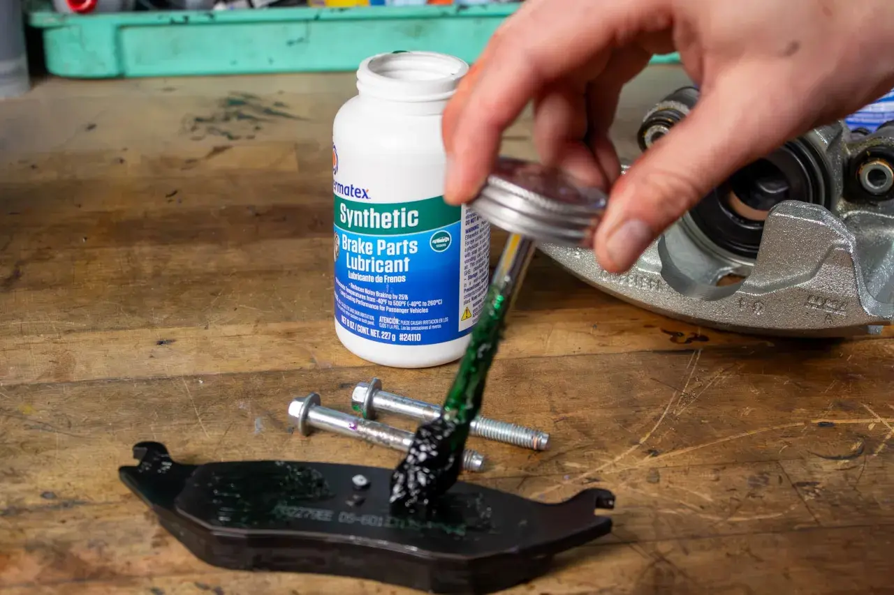 Nakładanie zielonego smaru do prowadnic hamulcowych z butelki "Synthetic Brake Parts Lubricant" na klocki hamulcowe i śruby.