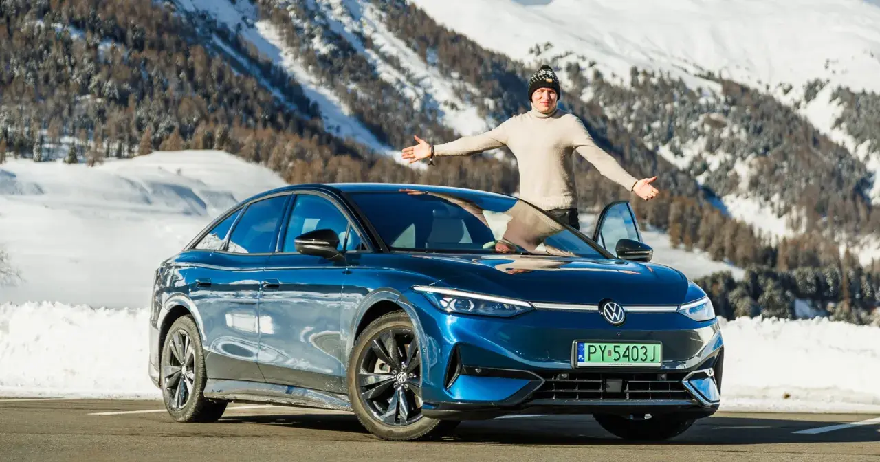Mężczyzna z otwartymi ramionami stoi obok lśniącego, niebieskiego VW ID.7 na tle ośnieżonych gór.