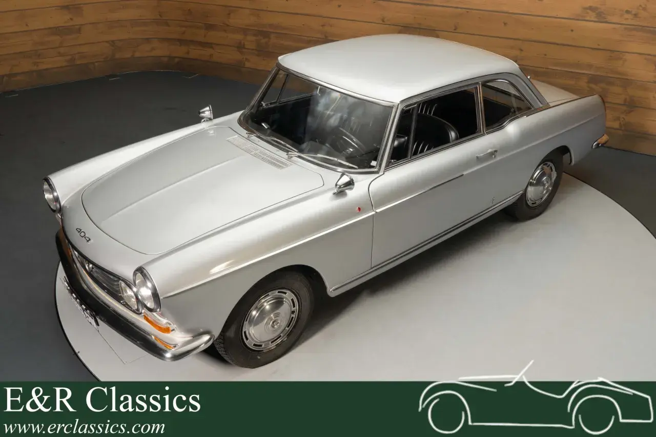 Elegancki, srebrny Peugeot 404 coupe z lat 60. na obrotowej platformie. Klasyka motoryzacji.