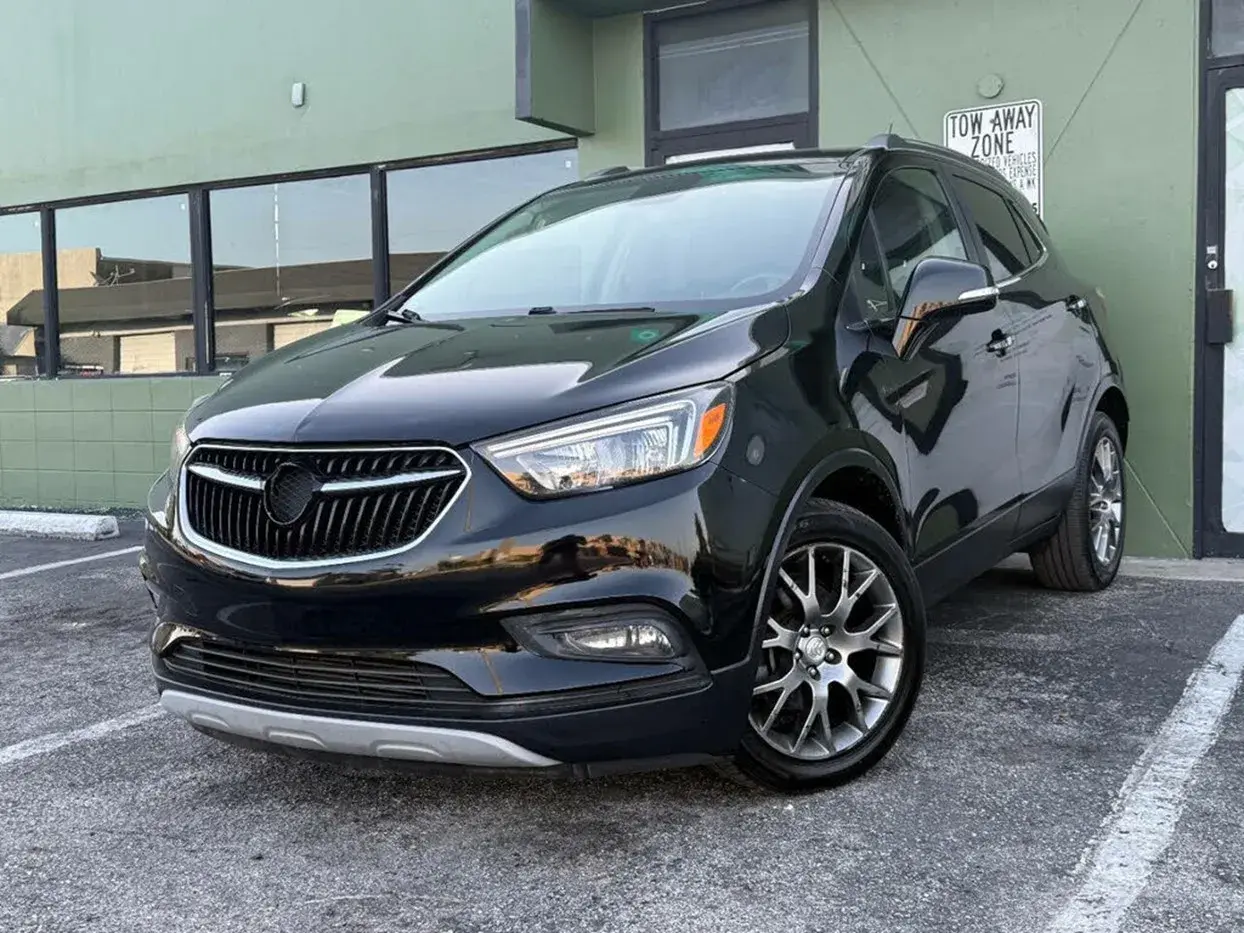 Czarny Buick Encore lśni w słońcu, zaparkowany przed zielonym budynkiem.