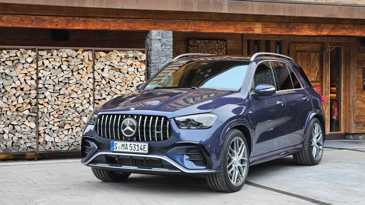 Elegancki, granatowy Mercedes GLE 53 AMG zaparkowany przed drewnianym domem z ułożonym drewnem.