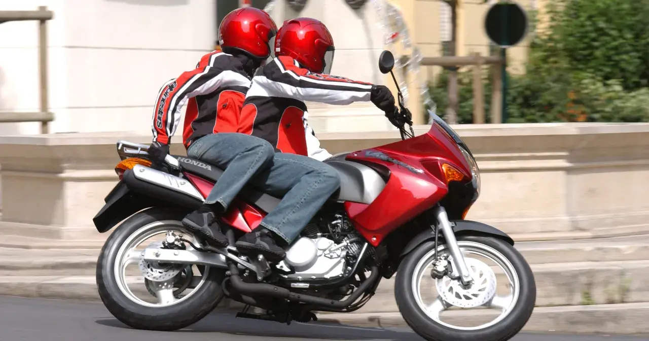 Dwie osoby w kaskach i kurtkach jadą na czerwonym motocyklu. To idealny sposób na zdobycie prawa jazdy na motor 125.