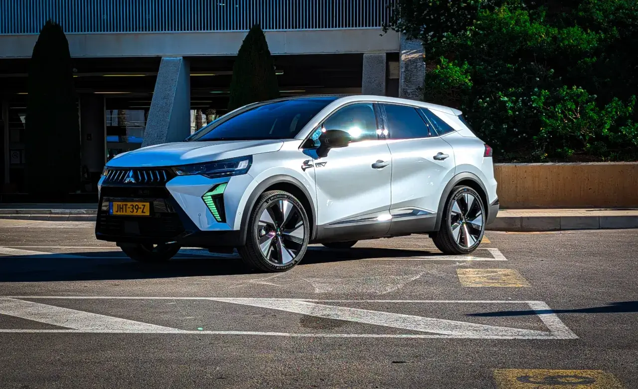 Nowy Mitsubishi Grandis w białym kolorze, zaparkowany na parkingu przed budynkiem.