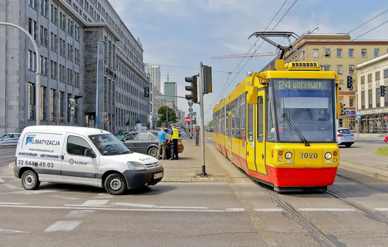 Żółty tramwaj z numerem 24 Gocławek ma pierwszeństwo na skrzyżowaniu, podczas gdy policjanci rozmawiają z kierowcą białego vana.