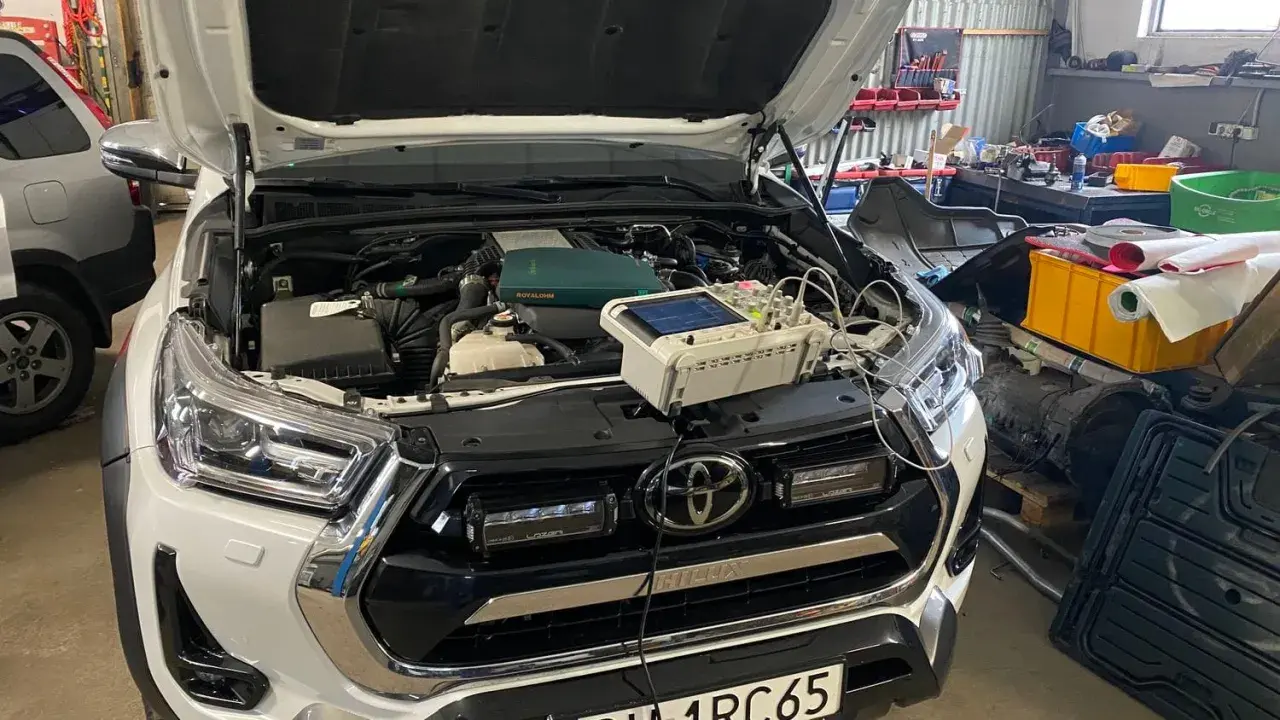 Biały Toyota Land Cruiser Prado w warsztacie, z otwartą maską i podłączonym sprzętem diagnostycznym.