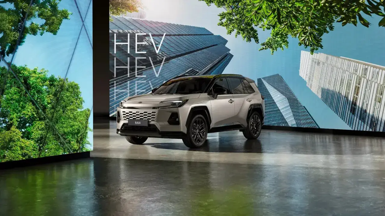 Srebrny SUV z napisem HEV na tle nowoczesnych budynków i zieleni.