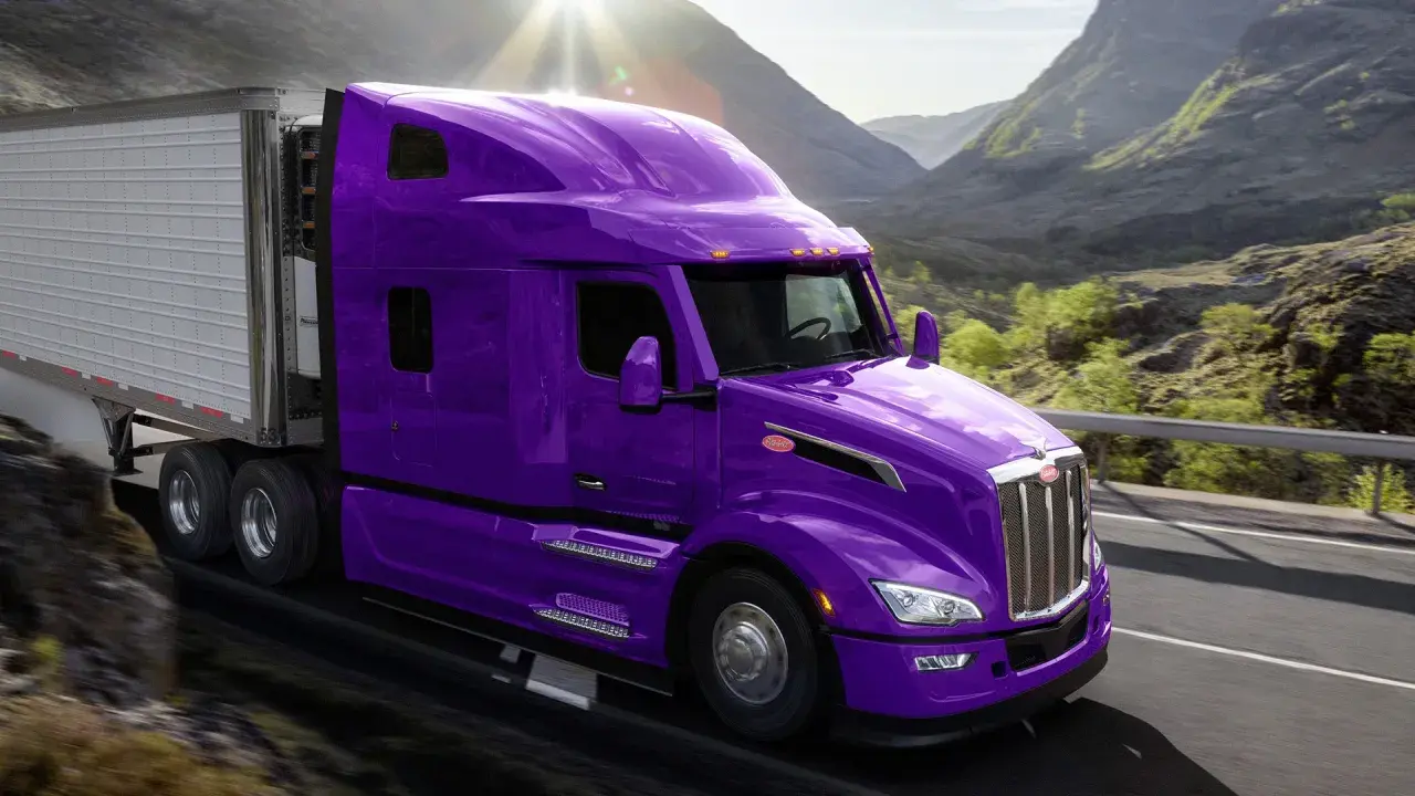 Fioletowy Peterbilt z naczepą pędzi przez górzysty krajobraz, oślepiony słońcem.