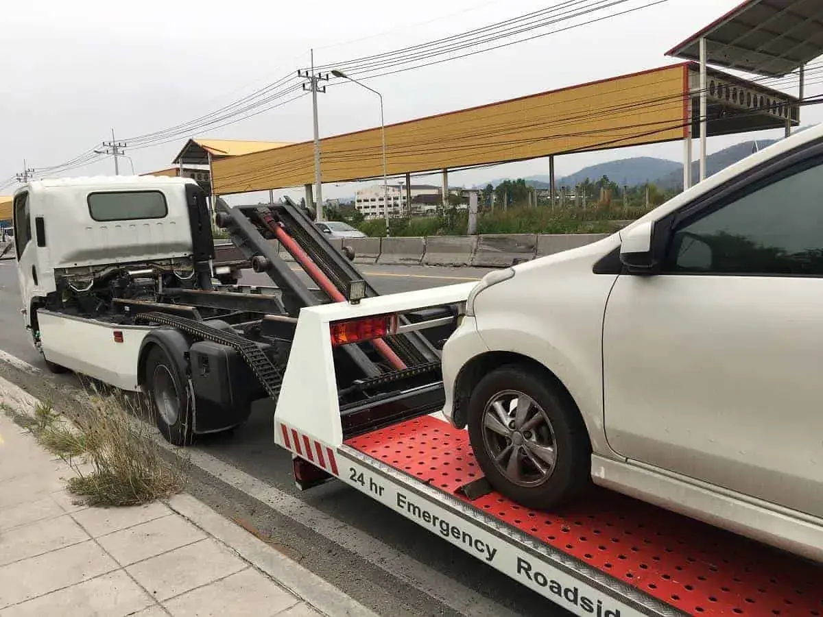 Pomoc drogowa w akcji: białe auto jest ładowane na lawetę. Widać mechanizm, jak holować auto, by bezpiecznie przetransportować pojazd.