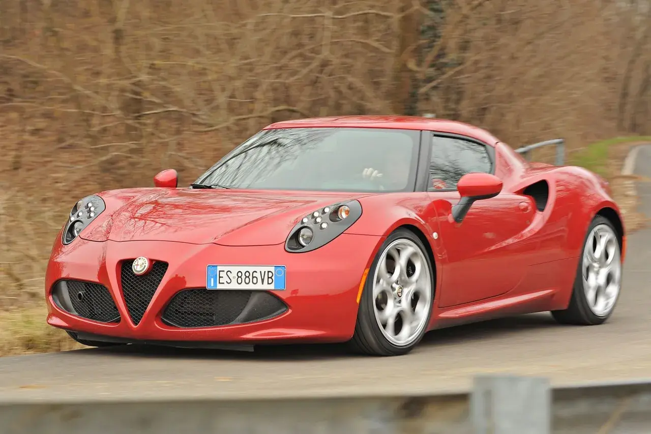 Czerwona Alfa Romeo 4C pędzi po krętej drodze, jej sportowy design przyciąga wzrok.
