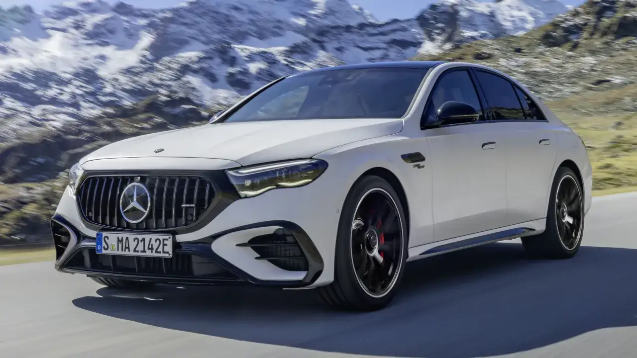Biały Mercedes-AMG E53 sedan pędzi po górskiej drodze, zaśnieżone szczyty w tle.