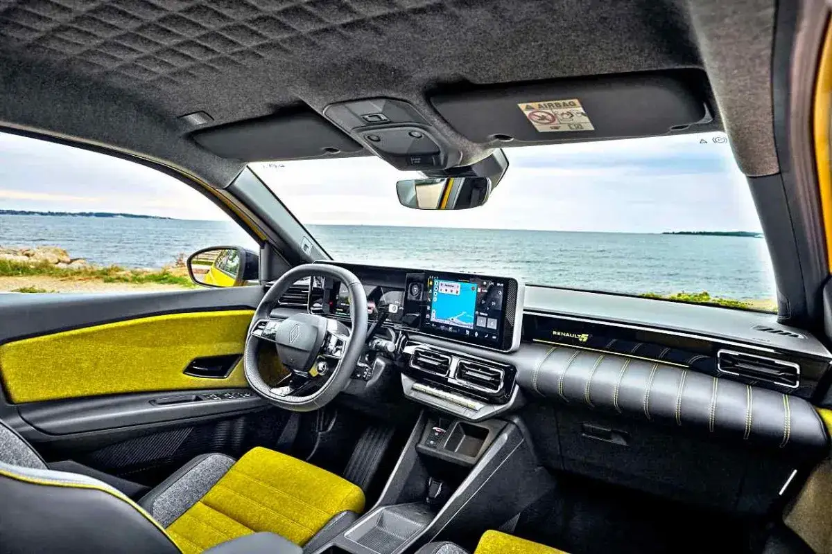 Wnętrze Renault 5 e-tech z żółtymi akcentami i ekranem nawigacji, widok na morze.