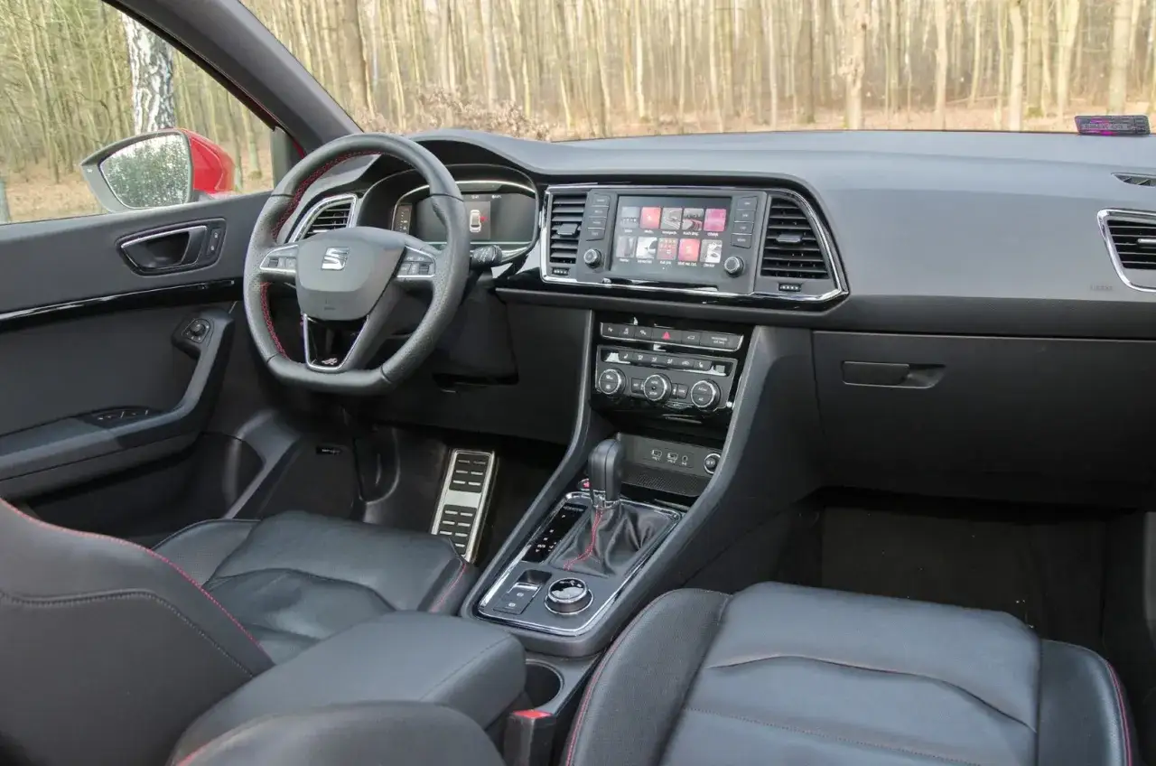 Wnętrze Seat Ateca FR z czarną skórzaną tapicerką i czerwonymi przeszyciami. Widoczny ekran multimedialny, kierownica i dźwignia zmiany biegów.