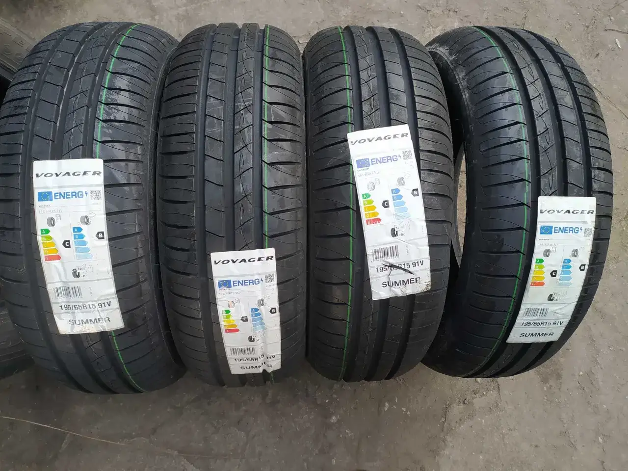 Cztery nowe opony letnie marki Voyager, rozmiar 195/65R15 91V, z etykietami energetycznymi.